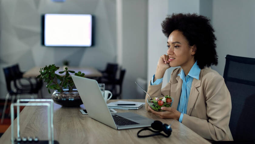 Mulher come salada em frente ao computador durante o trabalho