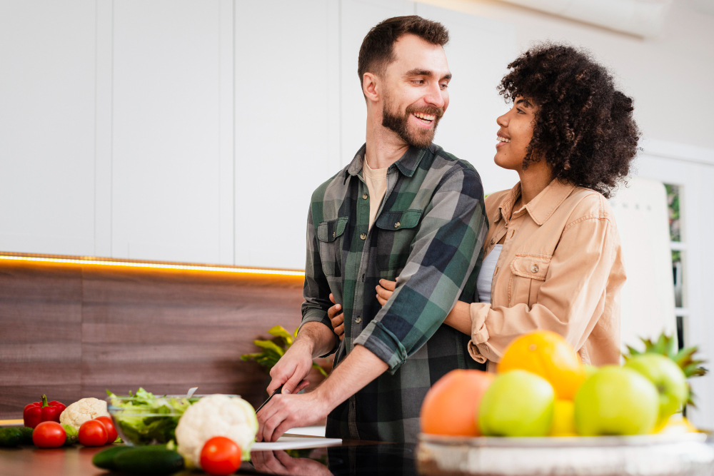 Homem prepara salada enquanto sorri para mulher que o abraça